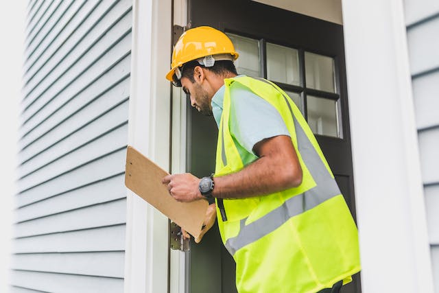 Person in a Neon Safety Vest and Checklist Inspeecting a Doorframe